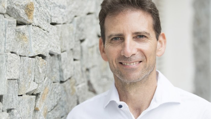 Headshot of Serge Benhayon standing alonside a brick paved wall